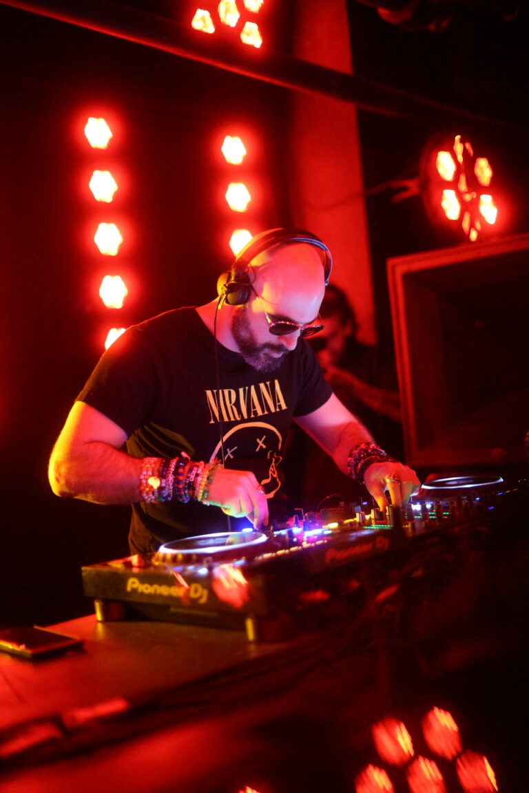 Company owner Mark Pompeo DJ'ing with a pair of CDJs and mixer in front of red-tinted club lights.