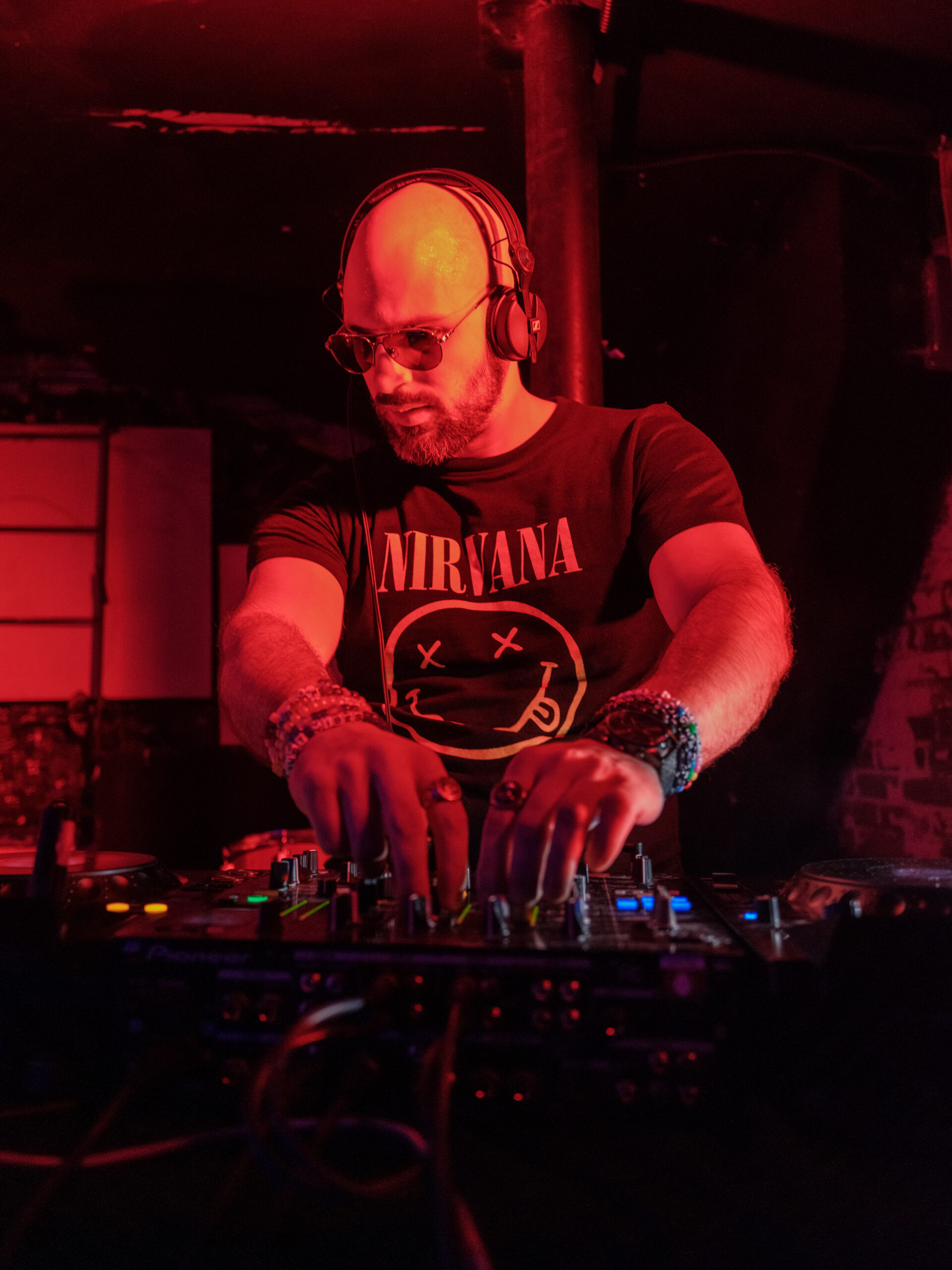 Company owner Mark DJ'ing, both hands on different knobs of the mixer, looking down and to the side towards a CDJ.