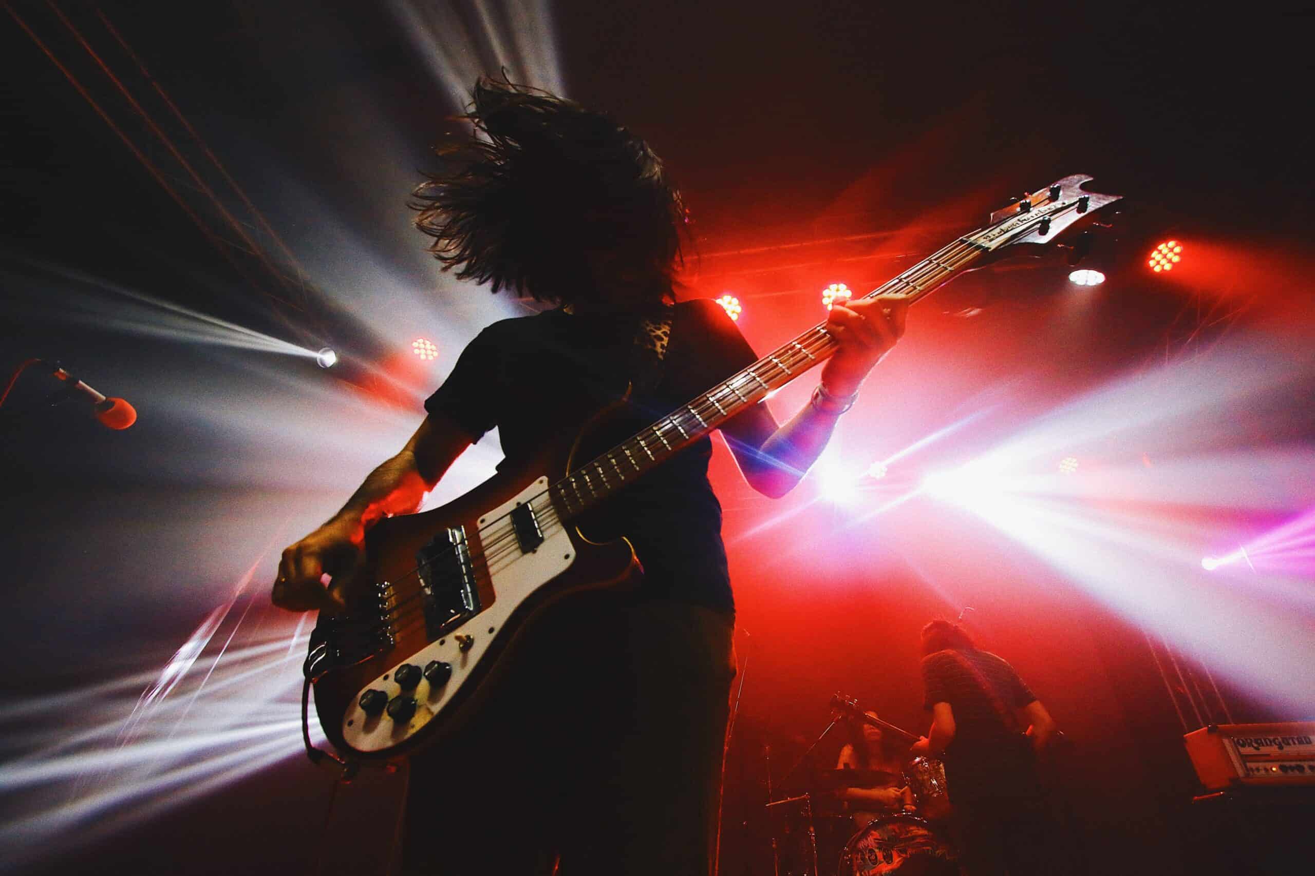 A bass player in a band during a concert on a stage with white and red lights
