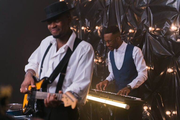 A guitarist and keyboard player performing in front of a black backdrop with lights