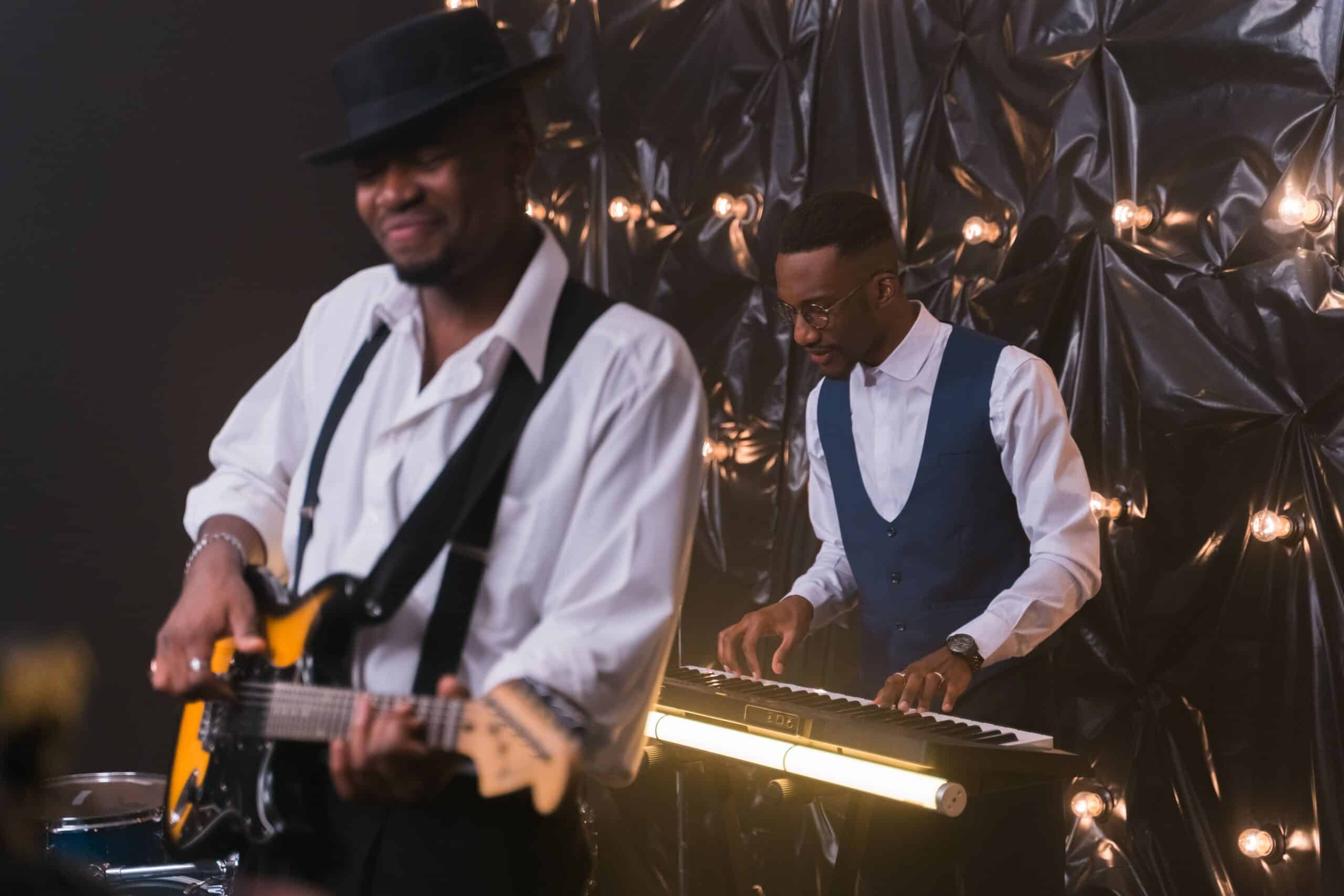 A guitarist and keyboard player performing in front of a black backdrop representing bands, musicians, and other music artists