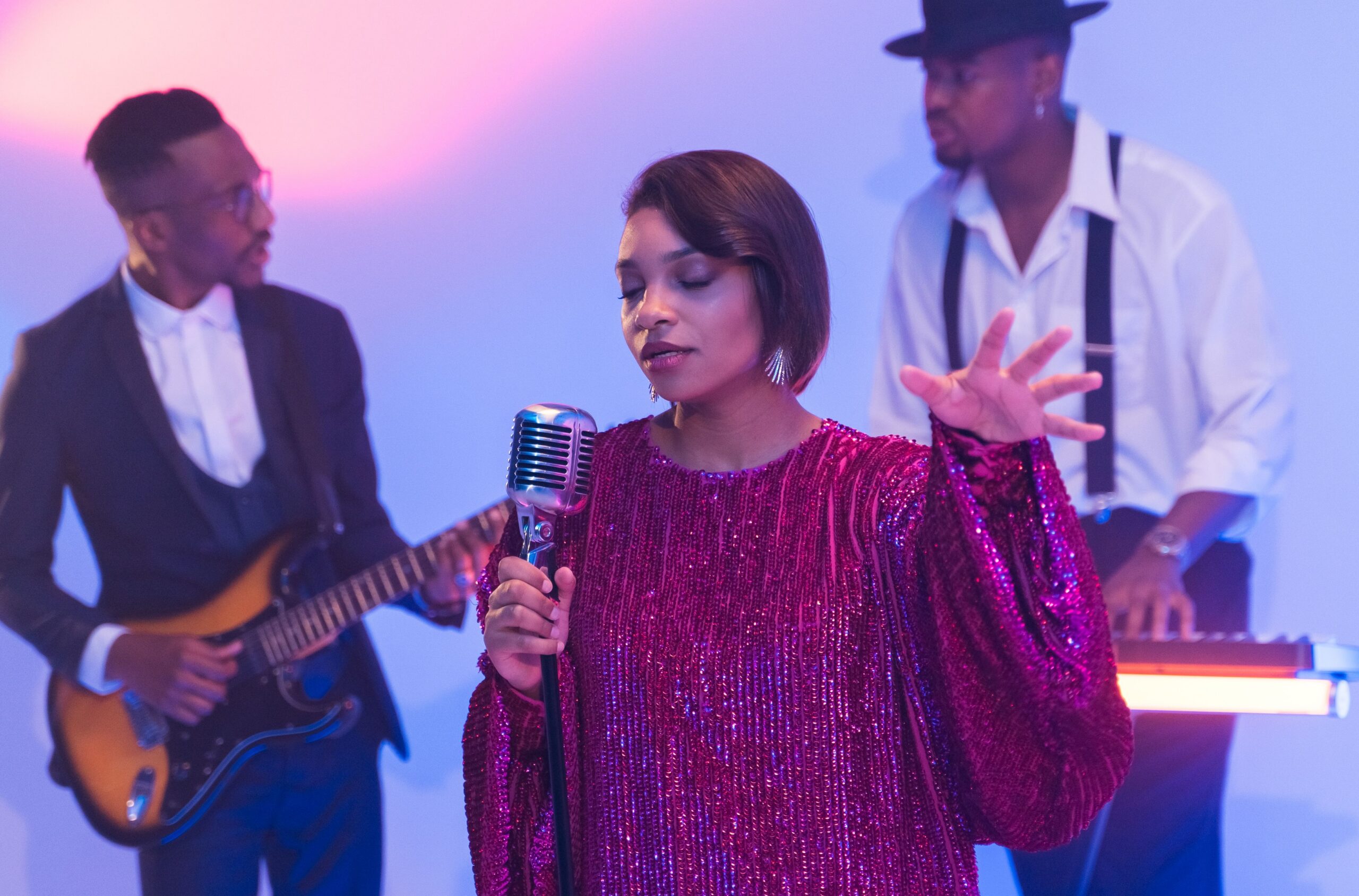 A singer, guitarist, and keyboardist performing in front of a pale blue backdrop.