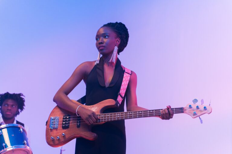 A female bass player with a male drummer behind in the lower left corner.