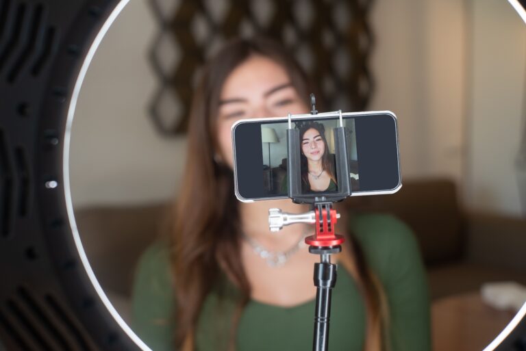 A social media influencer filming themselves with a cellphone and ring light.