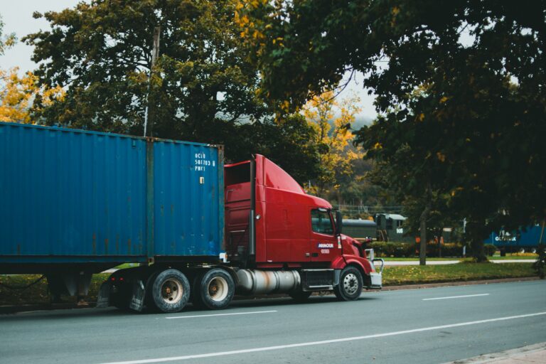 Freight truck on a local road in front of trees with a train in the background