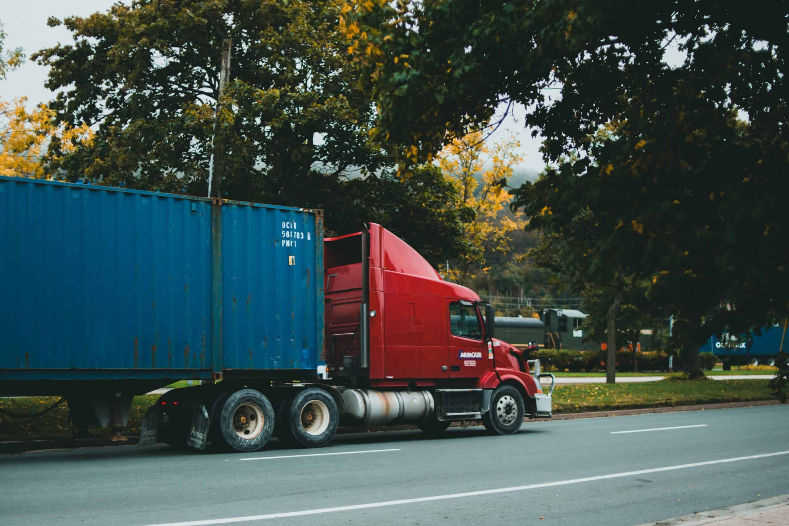 Freight truck on a local road in front of trees with a train in the background
